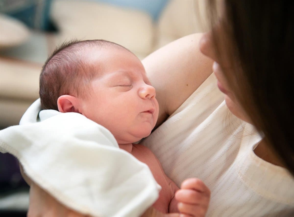 Maman berçant son nouveau-né endormi dans ses bras : frein de langue et biberon, un retour au sein reste possible