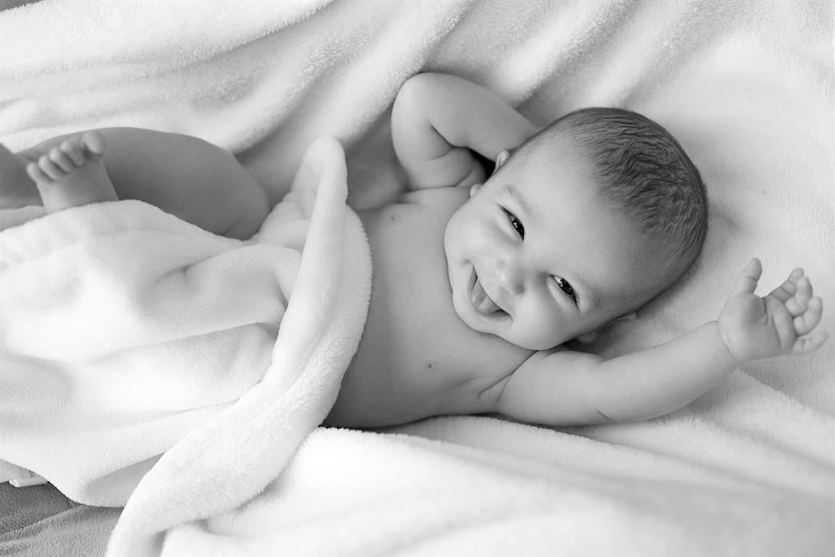 Bébé souriant sur une couverture douce : témoignages de parents après une frénectomie