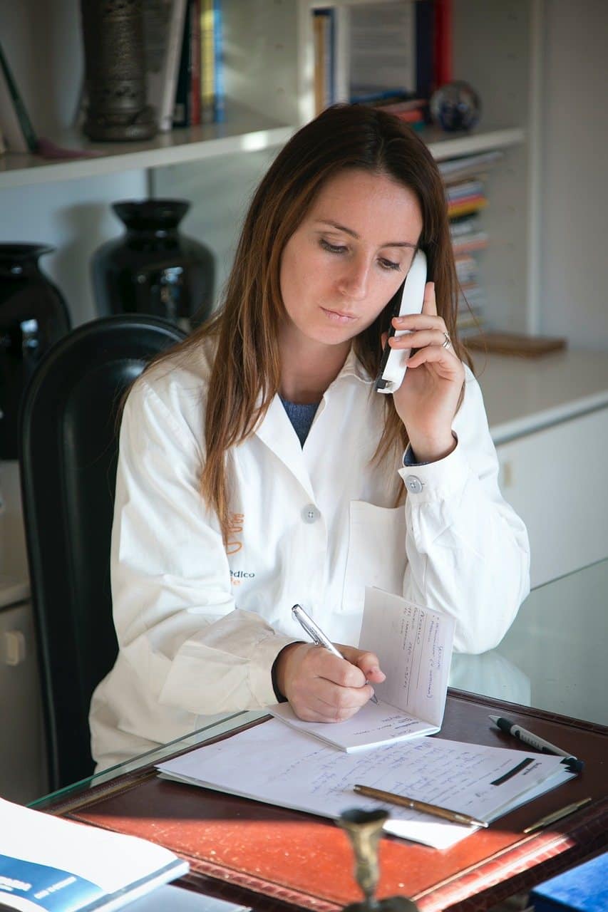 Professionnelle de santé en blouse blanche au téléphone : prendre rendez-vous pour une frénectomie